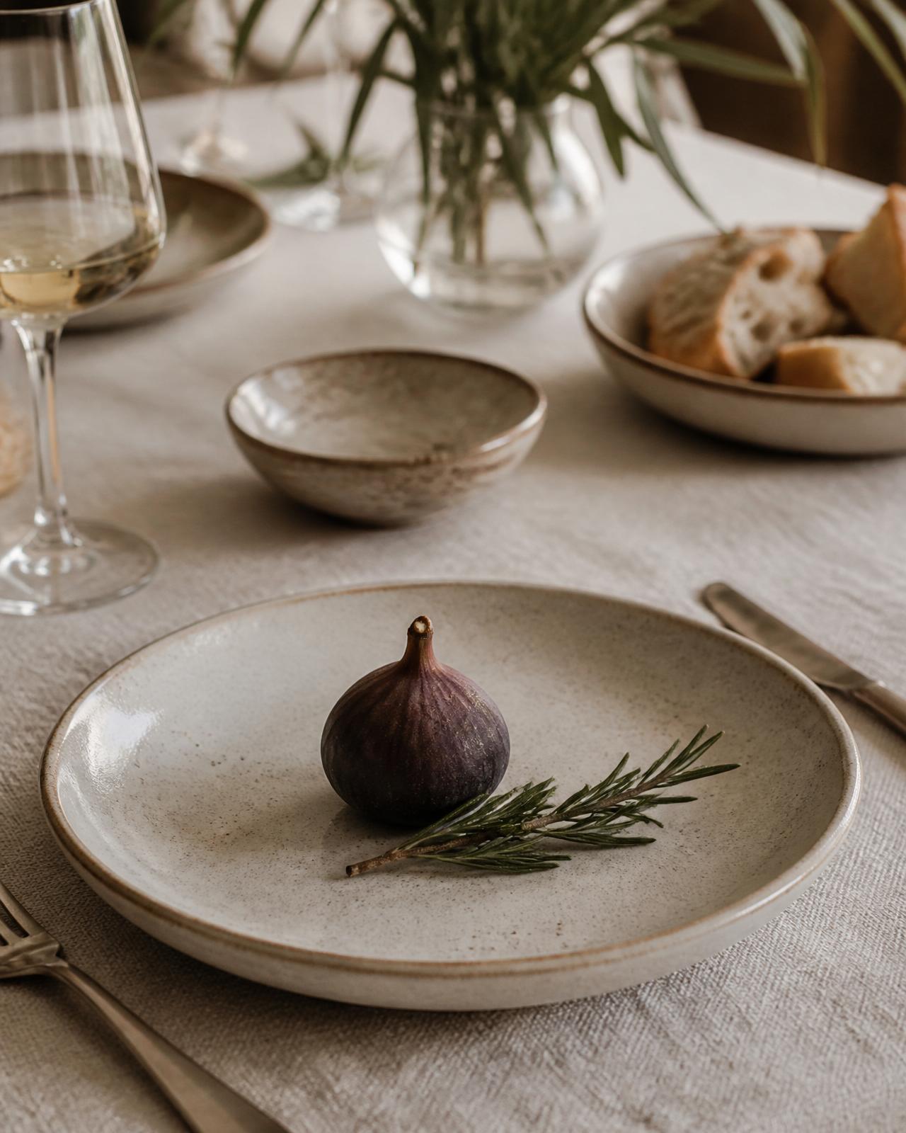 A quiet table set with linen, ceramic and a single fig